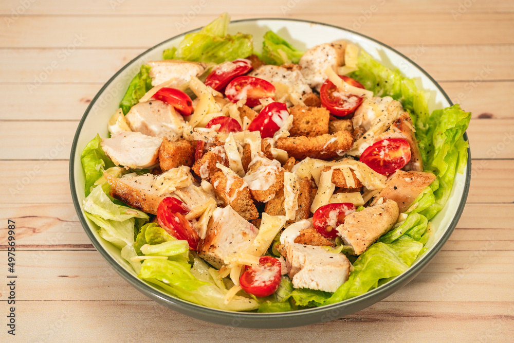 Exquisite variation of Caesar salad with small bites of chicken, cherry tomatoes and a gourmet aioli sauce in a small bowl on a table. High view. Exquisite variation of Caesar salad with small bites of chicken, cherry tomatoes and a gourmet aioli sauce in a small bowl on a table. High view.