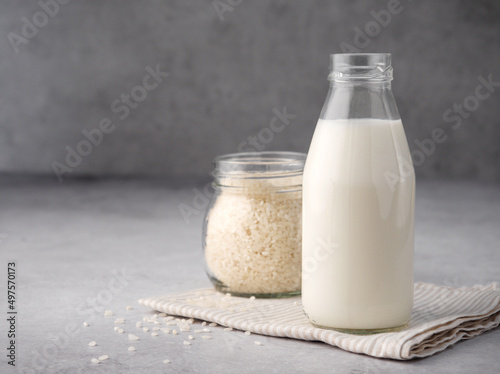 Vegan rice milk with rice grains on a gray concrete background. Copy space. Non dairy alternative milk. The concept of healthy vegetarian food and drinks. Diet healthy concept. Gluten-free breakfast.