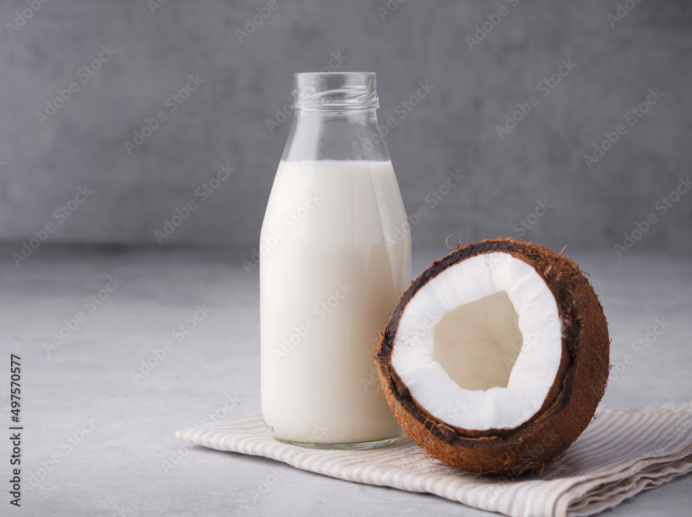 Coconut vegan milk is non dairy products in a bottle with a place to copy on a gray concrete background. Glass bottle of milk or yogurt with coconut chips aside. Concept of healthy eating. Close up. Coconut vegan milk is non dairy products in a bottle with a place to copy on a gray concrete background. Glass bottle of milk or yogurt with coconut chips aside. Concept of healthy eating. Close up.