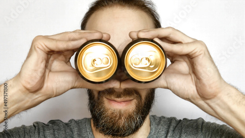 Bild auf Leinwand Close-up of a smiling bearded man putting two beer cans to his eyes imitating bi