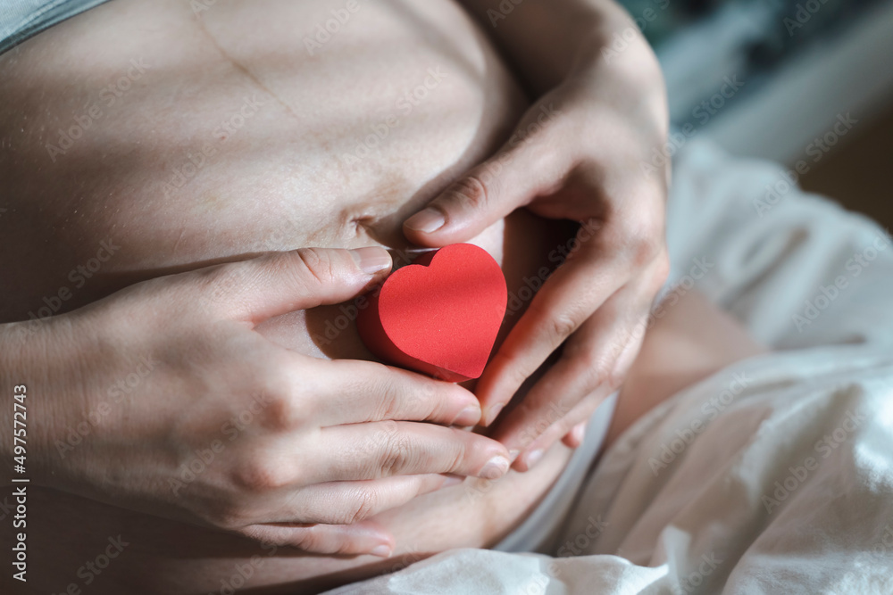 A pregnant woman after IVF holds a small red heart in her hands. The concept of motherhood, fertility, new life, In vitro fertilisation. Banner