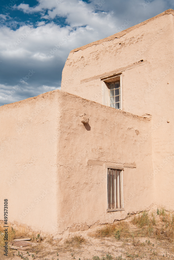 Corner view of two levels of an old adobe church with two rustic windows in Las Trampas, New Mexico