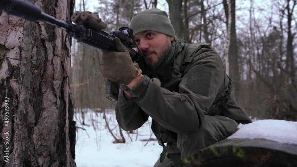 Portrait of young man with strikeball gun imitating shooting in slow motion outdoors. Handsome armed Ukrainian soldier in winter forest training. Lifestyle and defense concept Portrait of young man with strikeball gun imitating shooting in slow motion outdoors. Handsome armed Ukrainian soldier in winter forest training. Lifestyle and defense concept