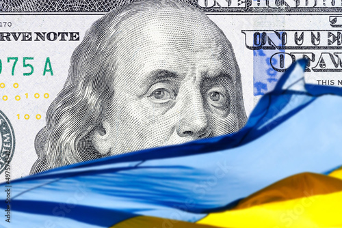 ukrainian national flag on foreground and US one hundred dollars paper currency on background. ukraine investment concept photo
