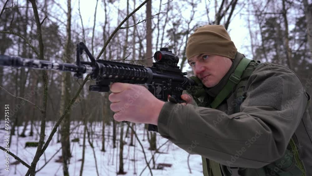 Serious focused military man aiming with gun walking in winter forest in slow motion. Portrait of concentrated Ukrainian soldier outdoors in war zone. Infantry and invasion concept