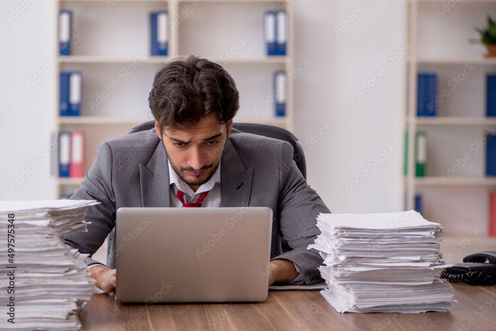 Young male employee unhappy with excessive work in the office Young male employee unhappy with excessive work in the office
