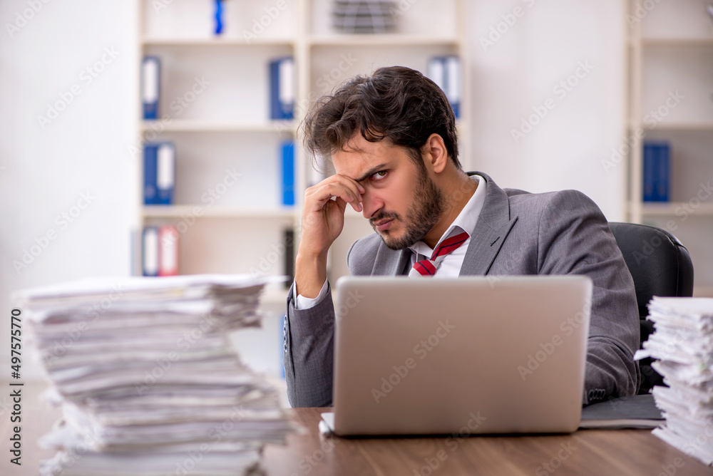 Young male employee unhappy with excessive work in the office Young male employee unhappy with excessive work in the office
