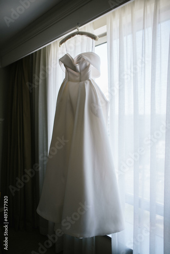 Wedding dress hanging in the room. Scenery for the morning of the bride with a white wedding dress and a bouquet. © Tobica
