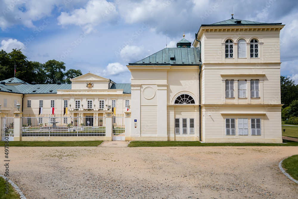 Lazne Kynzvart, West Bohemia, Czech Republic, 7 August 2021: Yellow and white Representative Chateau or summer castle in style of Viennese Classicism, green lawns, fountain in courtyard at sunny day