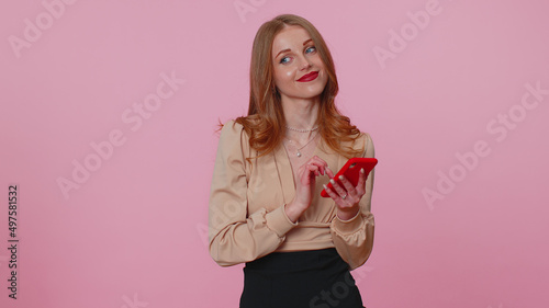 Businesswoman adult girl in beige blouse using mobile phone typing new post on web, sms message, browsing, addiction of social networks. Young fashionable woman indoors studio shot on pink background