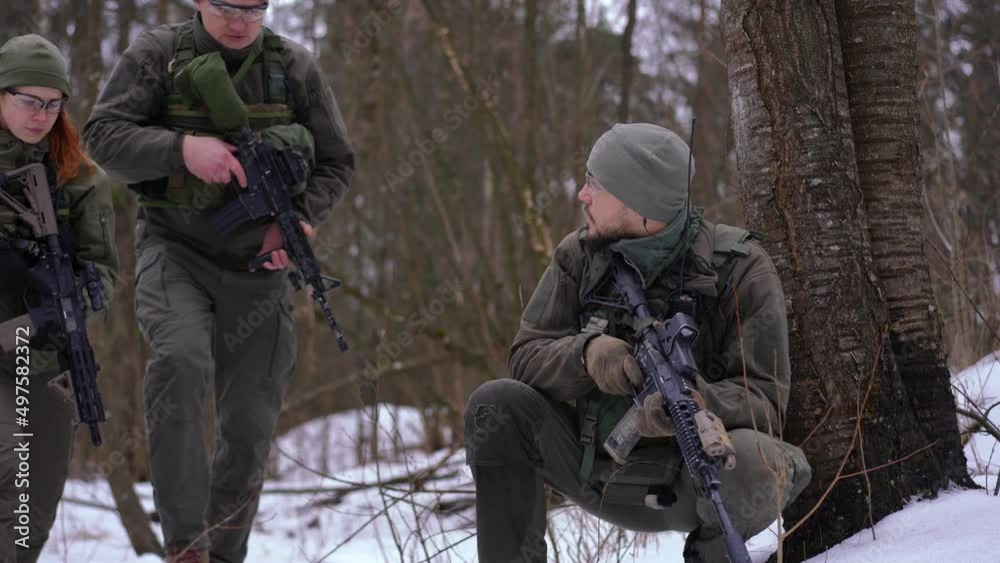Portrait of serious young handsome soldier gesturing as man and woman approaching with weapon. Concentrated Ukrainian armed defenders in snowy winter forest outdoors Portrait of serious young handsome soldier gesturing as man and woman approaching with weapon. Concentrated Ukrainian armed defenders in snowy winter forest outdoors