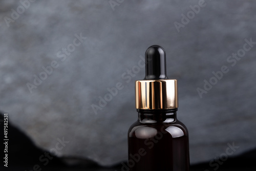 Brown bottle with dropper with a beauty serum granite stone on black background. Glass packaging for cosmetic product, essential aroma oil. Skin care, hydration and nutrition with collagen.