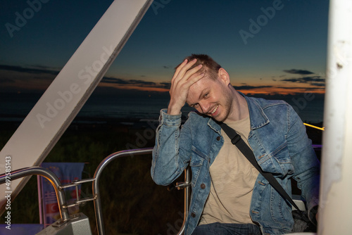 Beautiful shot of a Caucasian guy sitting on a Ferris wheel in the evening. photo