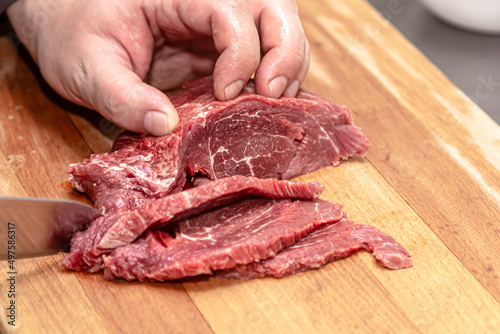The cook cuts the marbled beef into slices on a wooden board