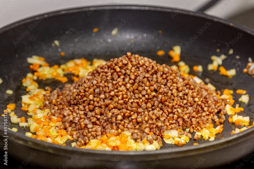 The cook cooks buckwheat porridge with onions and carrots in a frying pan The cook cooks buckwheat porridge with onions and carrots in a frying pan