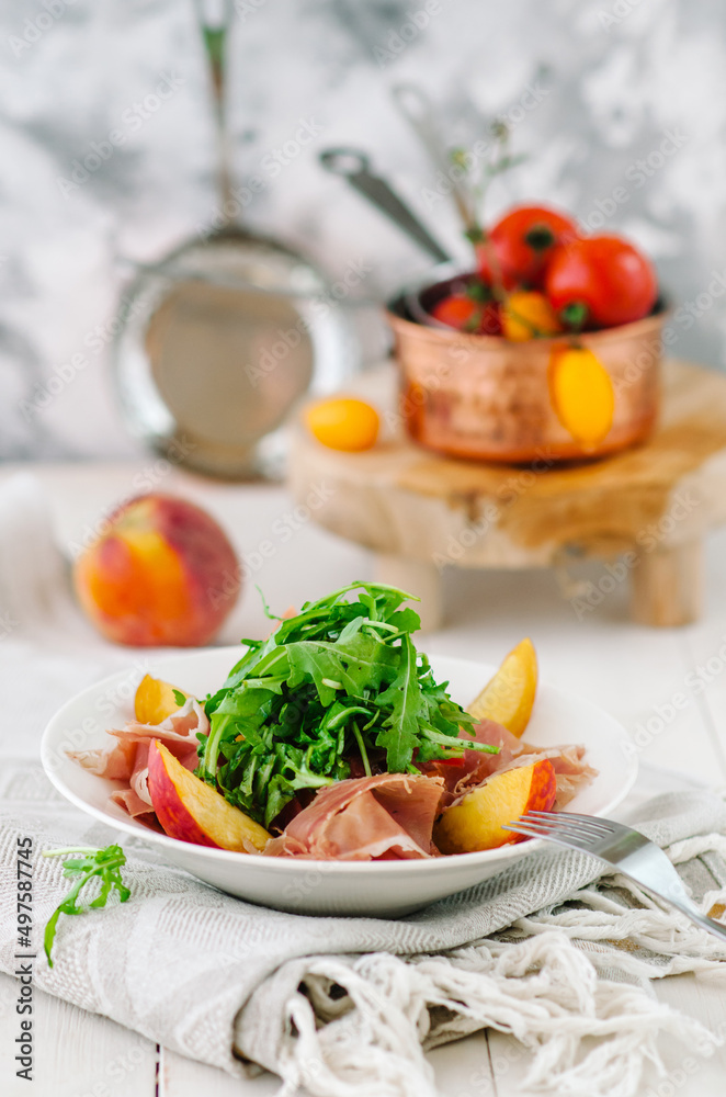 Salad bowl with grilled peach, prosciutto, goat cheese, walnuts and arugula on white background, top view, copy space
