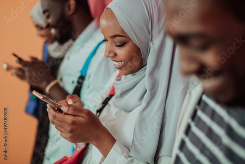 A group of African Muslim students use smartphones while standing in front of a yellow background