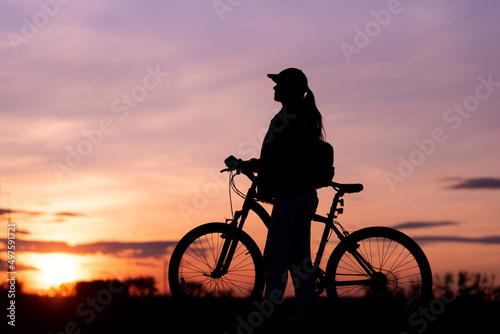 Bicycle rider silhouette with sunset sky in background, girl riding her bike staring at the sunny evening sky