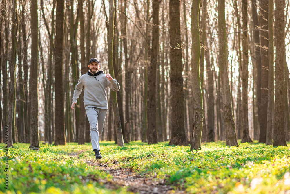 bearded young male wearing grey clothes does outdoors running outside in a sunny spring forest along pathway bearded young male wearing grey clothes does outdoors running outside in a sunny spring forest along pathway
