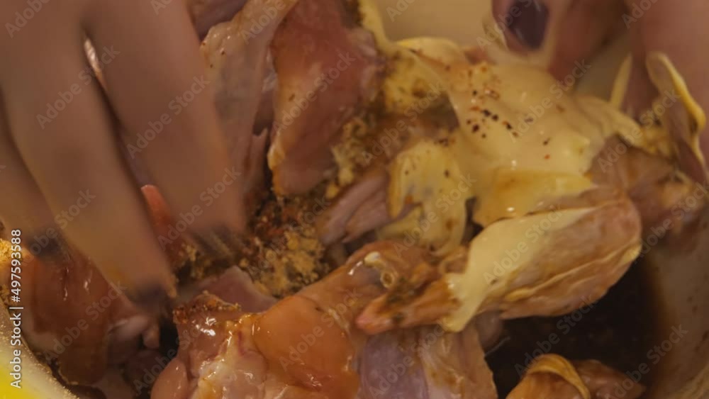 A woman's hand stirs marinated chicken wings in a large dish. Medium plan A woman's hand stirs marinated chicken wings in a large dish. Medium plan