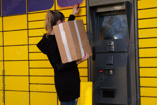 Beautiful woman picking up a package from a smart electronic steel parcel locker box, automatic mailboxes. Paczkomat delivery service, collection machine.