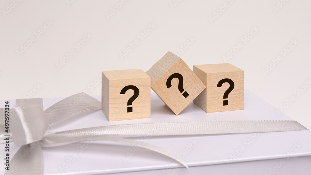 three cubes with question marks on the white surface of a gift box tied with a light festive ribbon three cubes with question marks on the white surface of a gift box tied with a light festive ribbon