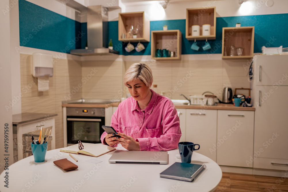 Short haired woman using smartphone in the kitchen at home Short haired woman using smartphone in the kitchen at home
