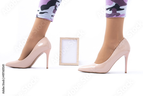 Slender female legs. Elegant patent beige high heels. Leggings in camouflage. The girl is standing sideways. frame with place for text. A combination of strength and femininity. The concept of female