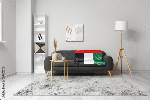 Interior of light living room with black sofa, shelving unit and UAE flags