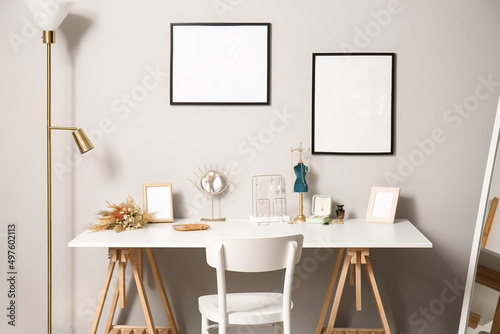 Stylish jewelry on table and blank photo frames on light wall in room © Pixel-Shot