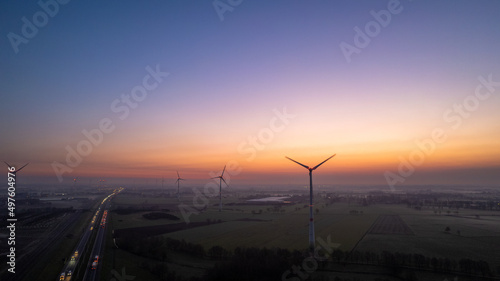 Aerial view sunrise of meadows and electric windmills across high speed highway on the morning under a colorful sky natural landscape over the panorama landscape. High quality photo