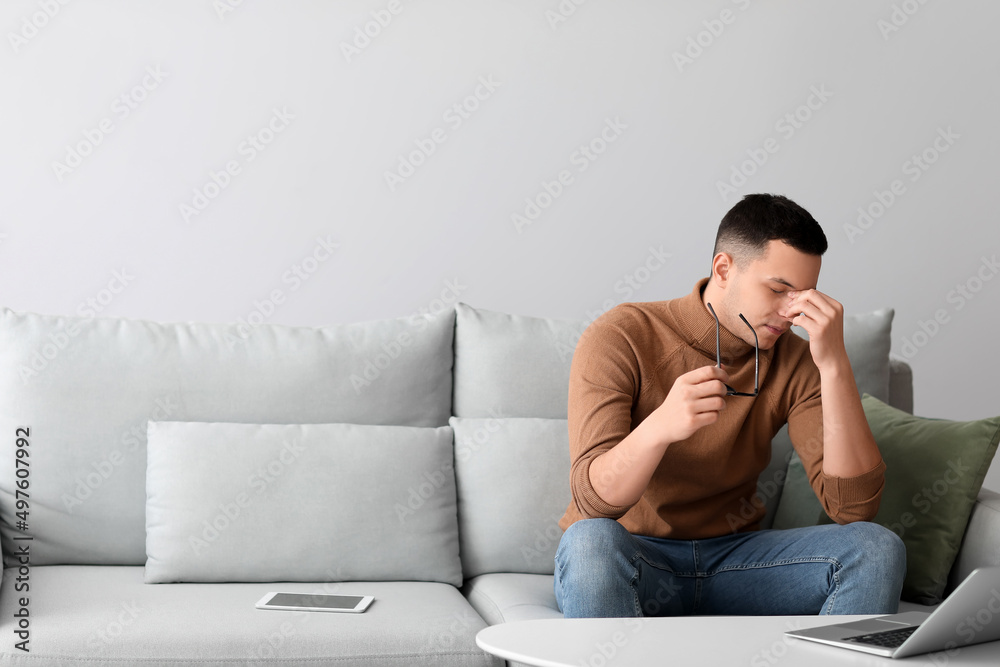 Worried young man with eyeglasses sitting on sofa at home Worried young man with eyeglasses sitting on sofa at home