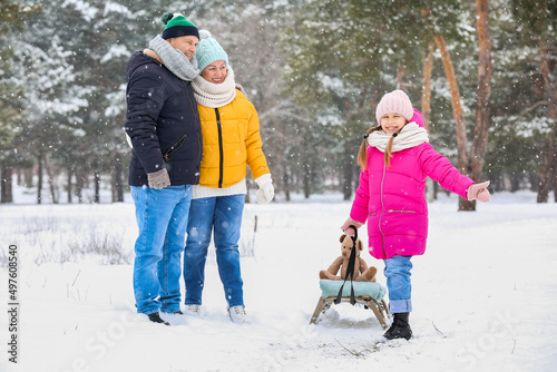 Little girl with sledge and her grandparents on snowy winter day