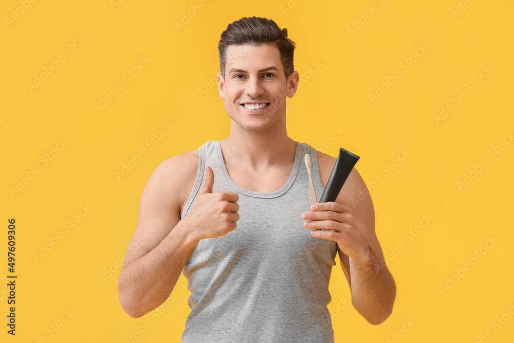 Handsome young man with activated charcoal tooth paste and brush showing thumb-up on yellow background Handsome young man with activated charcoal tooth paste and brush showing thumb-up on yellow background