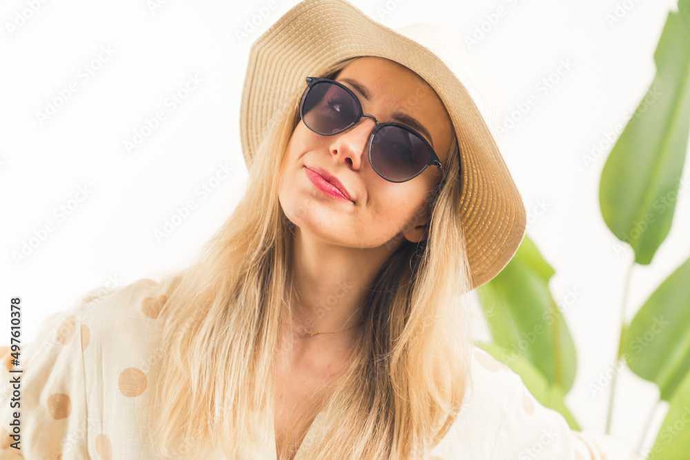 lovely Caucasian blonde girl with black sunglasses and hat looking into the camera white background with green leaves medium closeup studio shot copy space. High quality photo lovely Caucasian blonde girl with black sunglasses and hat looking into the camera white background with green leaves medium closeup studio shot copy space. High quality photo