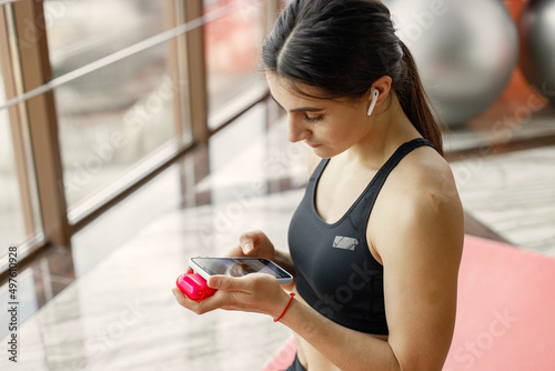 Fitness girl sitting on a yoga mat and using a wireless earphones