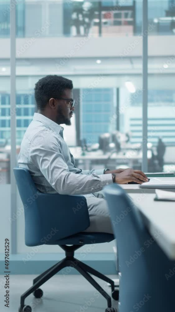 Vertical Screen: African American Business Manager Using Computer in Office, Businesspeople and Experts Working Around Him, Analysing Statistics, Commerce Data, Marketing Plans. Zoom In Portrait. Vertical Screen: African American Business Manager Using Computer in Office, Businesspeople and Experts Working Around Him, Analysing Statistics, Commerce Data, Marketing Plans. Zoom In Portrait.