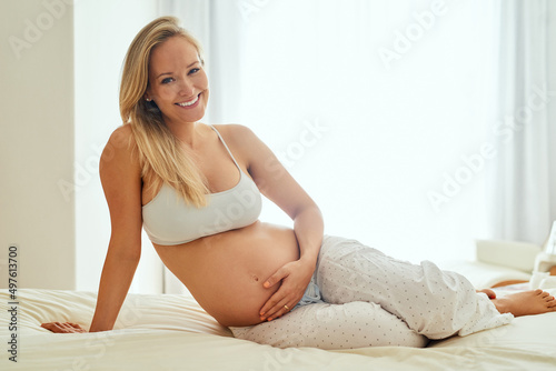 Happy mamas make happy babies. Shot of a pregnant woman touching her belly while sitting on her bed. photo