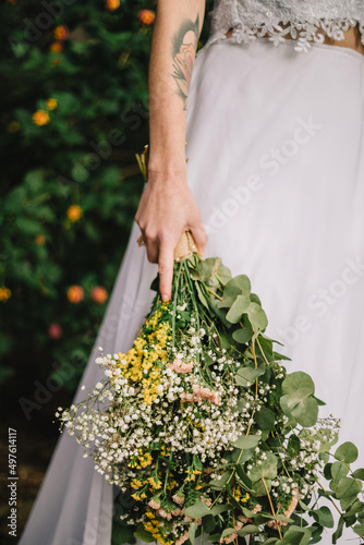 Vertical shot of a beautiful Caucasian bride with a white dress  holding a bouquet in the garden