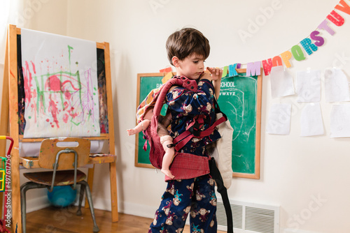 boy wears toy baby doll in baby carrier photo