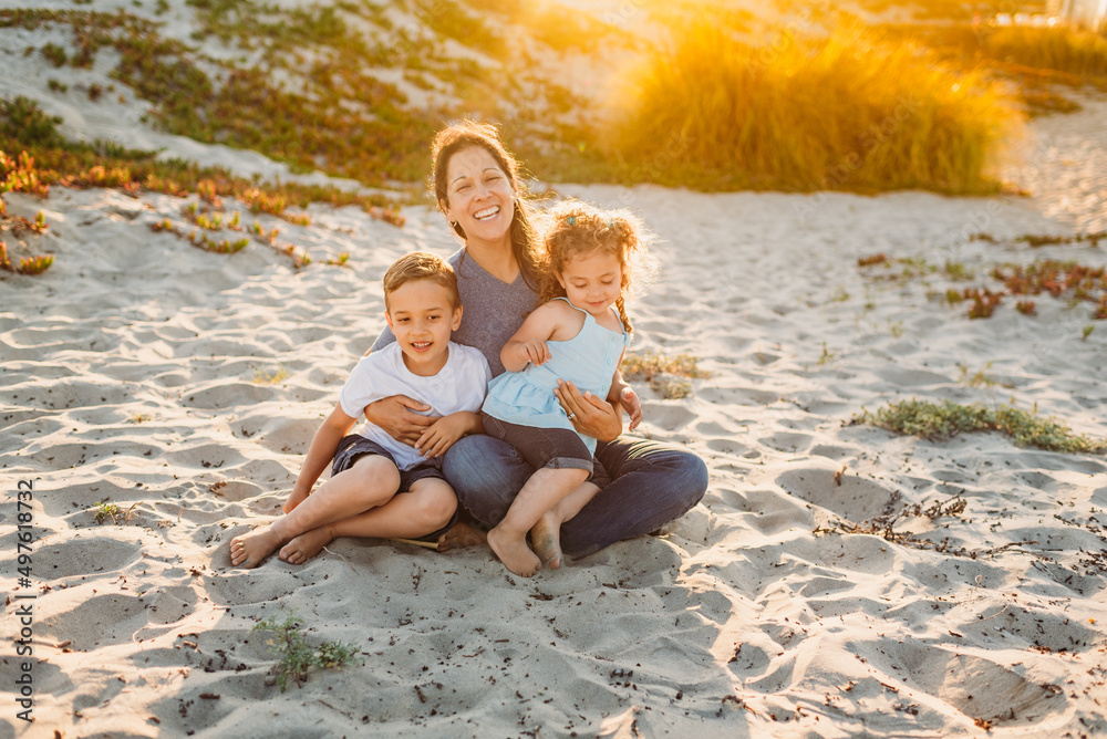 Smiling mom with kids sitting on lap at beach