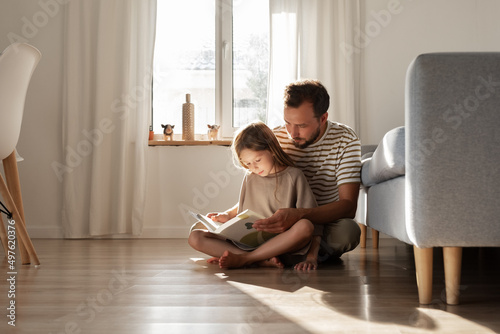 Father and daughter reading book on floor photo