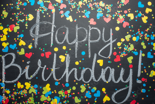 An inscription with a birthday on a blackboard, framed with colored confetti. View from above