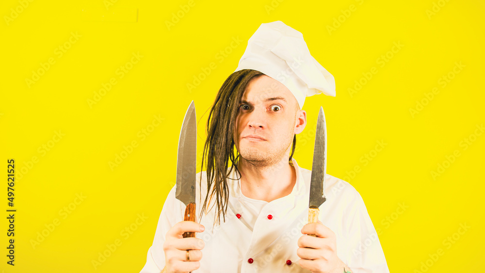 Young insane man dressed as chef with knives on yellow background. Crazy male cook in white hat and shirt posing with kitchen knives. Young insane man dressed as chef with knives on yellow background. Crazy male cook in white hat and shirt posing with kitchen knives.