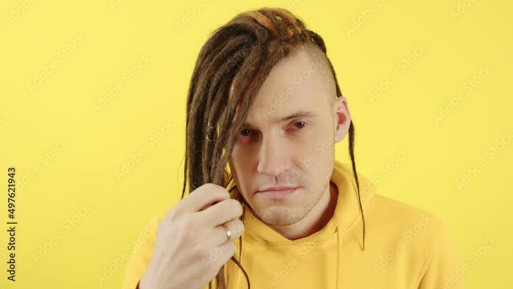 Young man twisting hair and looking at camera on yellow background. Handsome guy with modern hairstyle, dreadlocks posing in studio. Young man twisting hair and looking at camera on yellow background. Handsome guy with modern hairstyle, dreadlocks posing in studio.