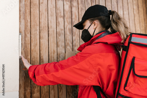 Delivery woman with food backpack ringing doorbell photo