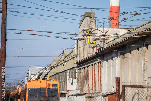 Power pole and pantograph of a trolleybus connecting vehicle to electrical cable line, the overhead cable, or catenary in a neglected industrial background in a worskhop depot. ..