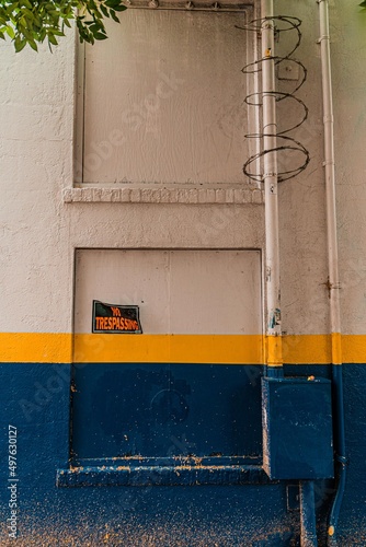 Grungy, Distressed blue and Yellow striped wall with Barbed Wire and No Trespassing Sign  San Diego, California © Brian