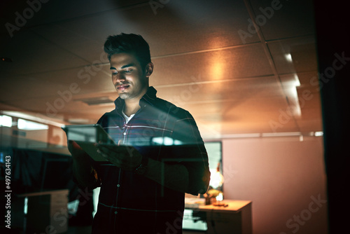 All nighters are nothing for a get it done guy. Shot of a young businessman using a digital tablet during a late night at work. photo