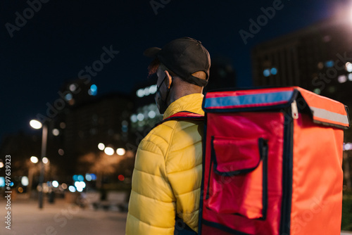 Anonymous delivery man with backpack carrying order in city photo